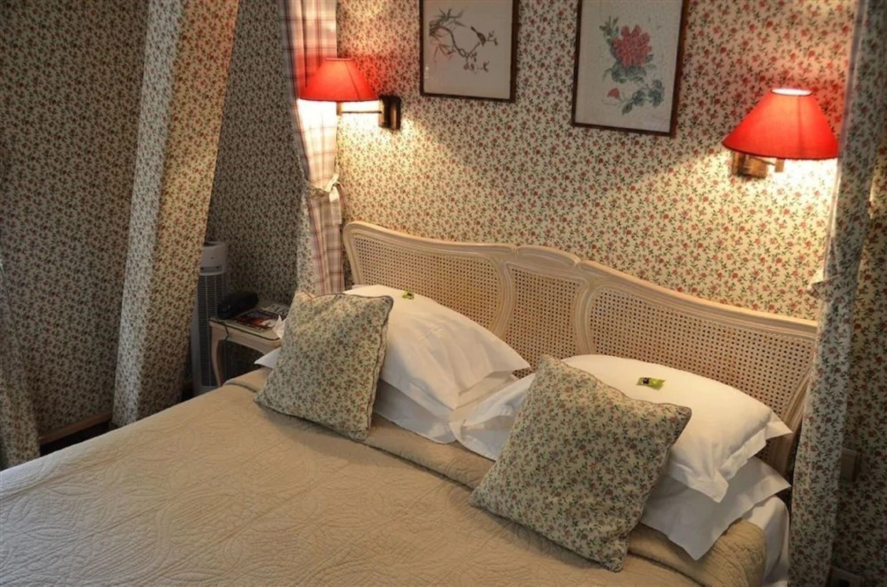 Una cama con almohadones estampados, cabecera y dos lámparas fijadas a la pared.