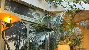 Un coin salon accueillant avec un canapé en osier et une table basse en verre, entouré d’une végétation luxuriante et agrémenté d’une grande fresque murale.