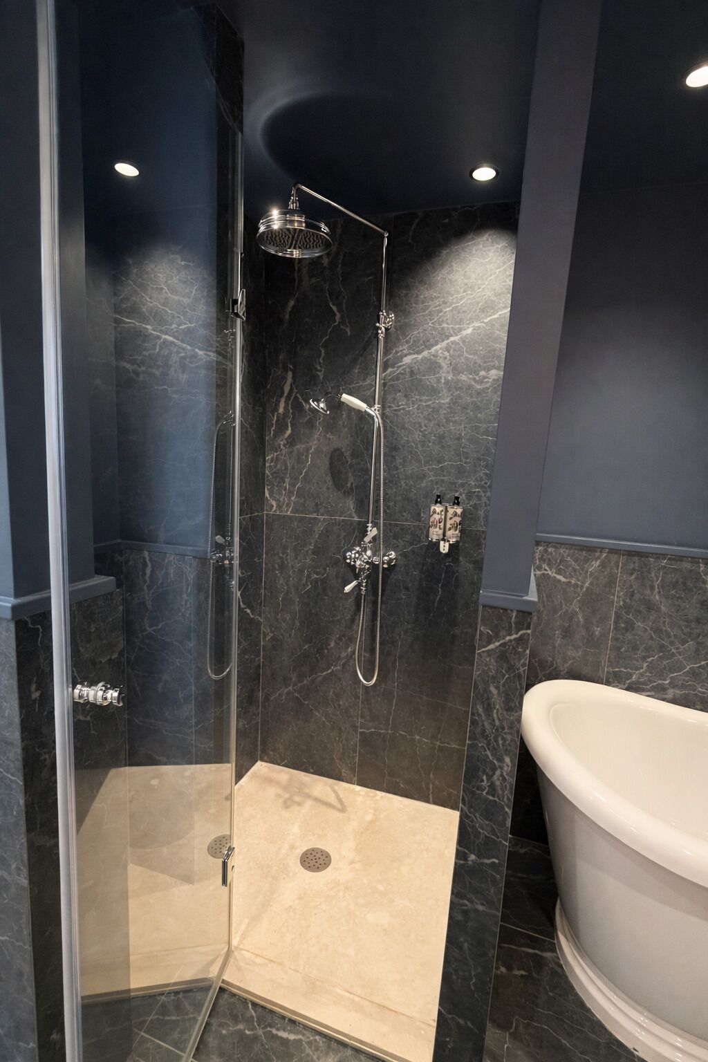 A modern bathroom with a glass-enclosed shower, a freestanding bathtub, and marble walls.