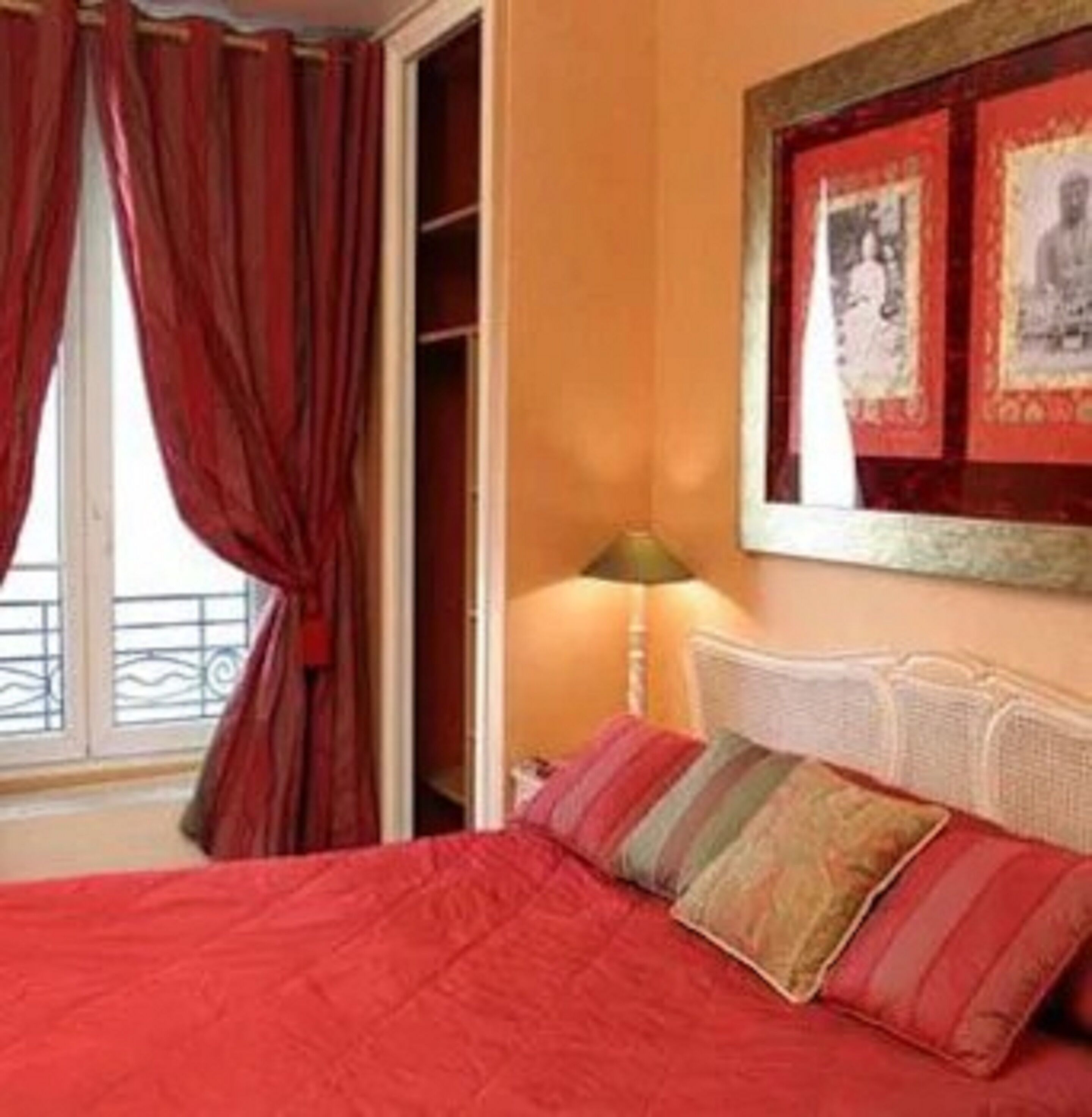 Een hotelkamer met een bed, rode gordijnen, een raam met uitzicht en een muur met ingelijste foto's.