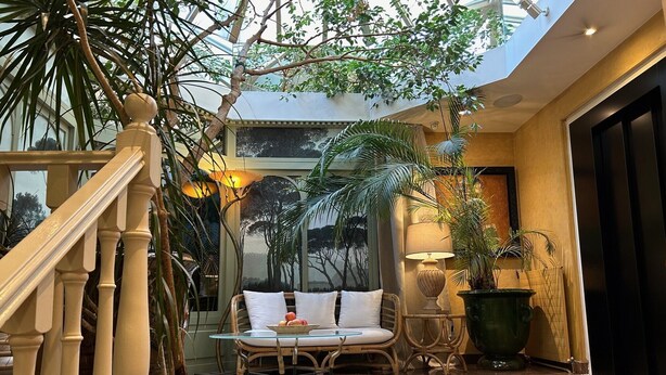 Un vaste atrium intérieur doté d’un haut plafond, d’un espace de détente central avec une table ronde et d’un escalier avec des balustrades en bois.