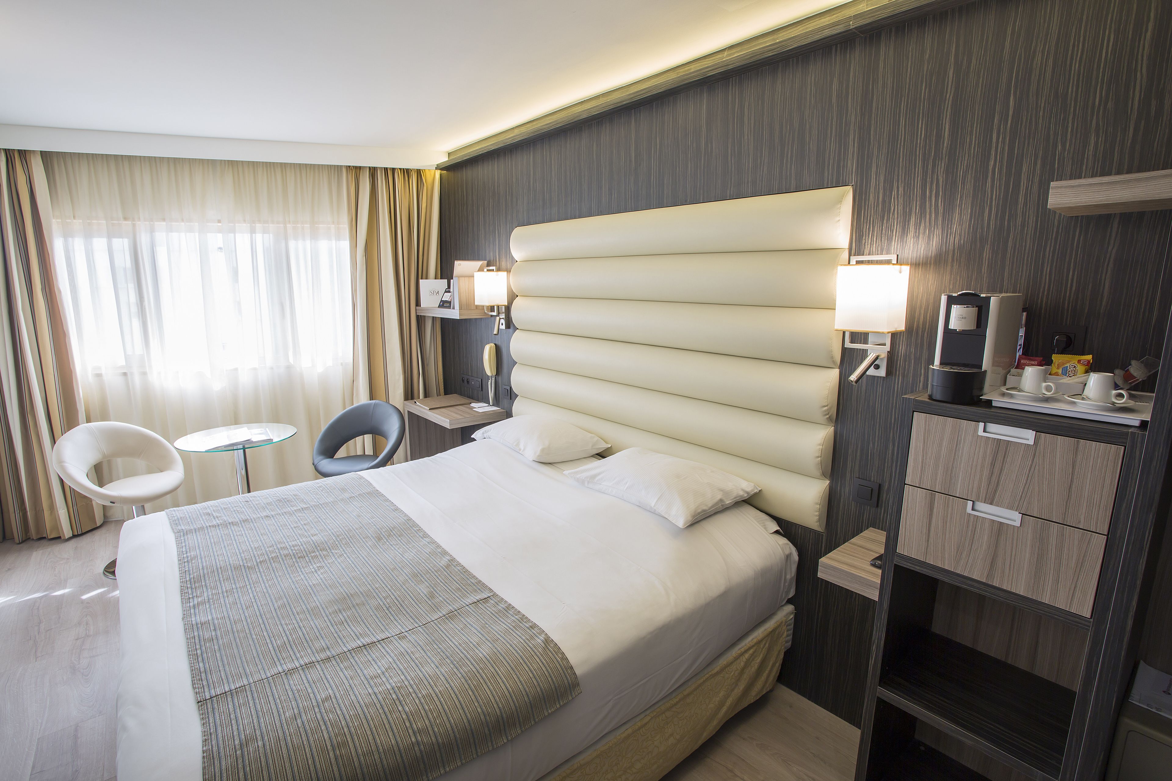 A hotel room with a large bed, two bedside tables, a chair, a desk, and a minibar.