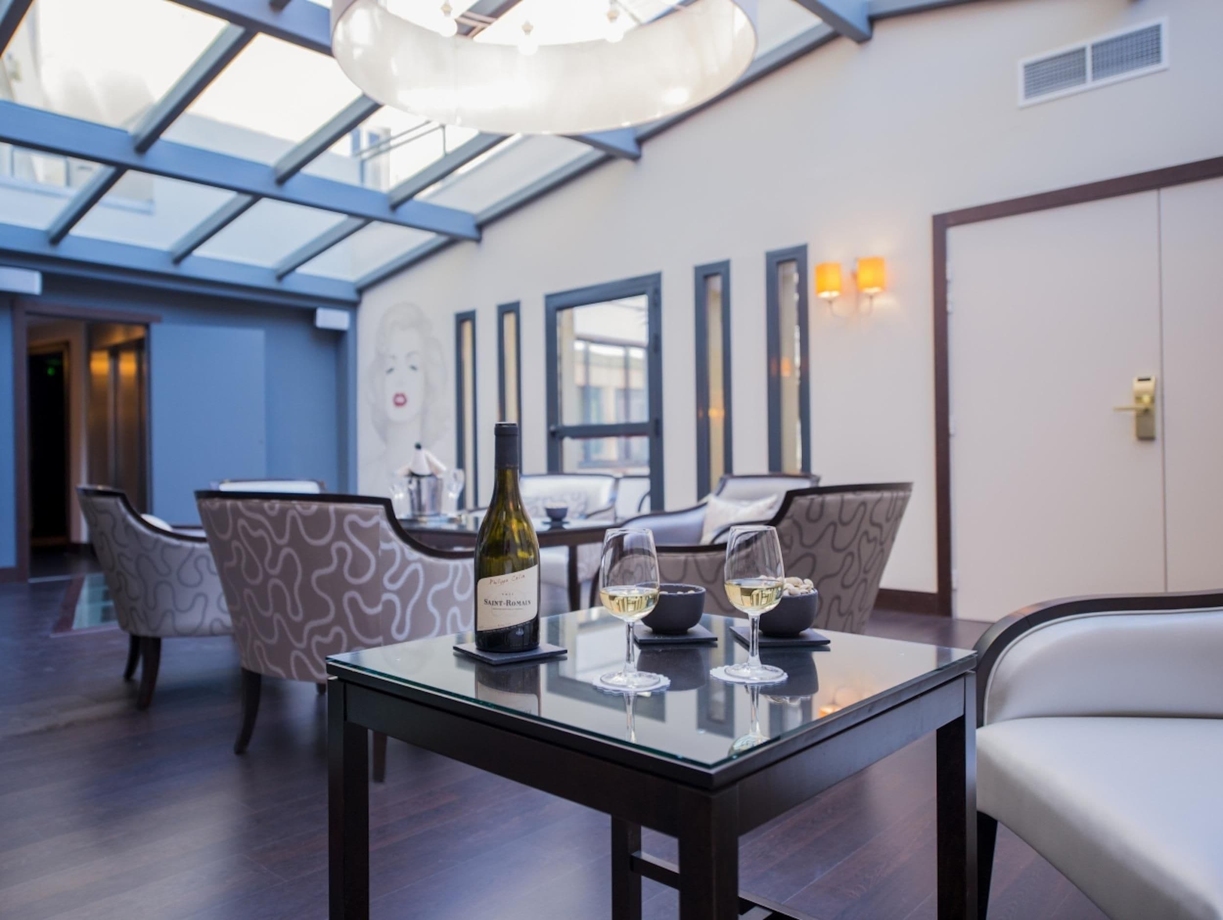 A modern dining area with a glass table, chairs, and a bottle of wine.