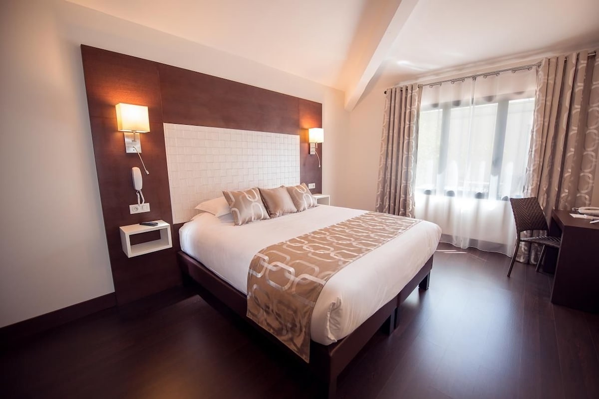 A hotel room with a large bed, bedside lamps, a desk, and a chair.