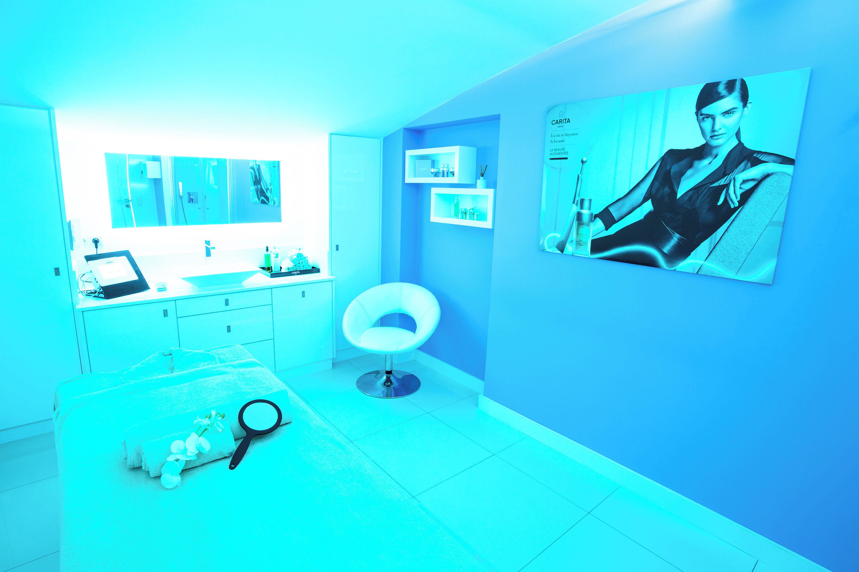 Une salle de bain moderne aux tons bleus, avec un meuble-lavabo blanc, un miroir rond et une grande affiche accrochée au mur.
