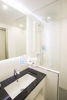 Un baño moderno con un lavabo blanco, un espejo grande y una ducha con mampara de cristal.