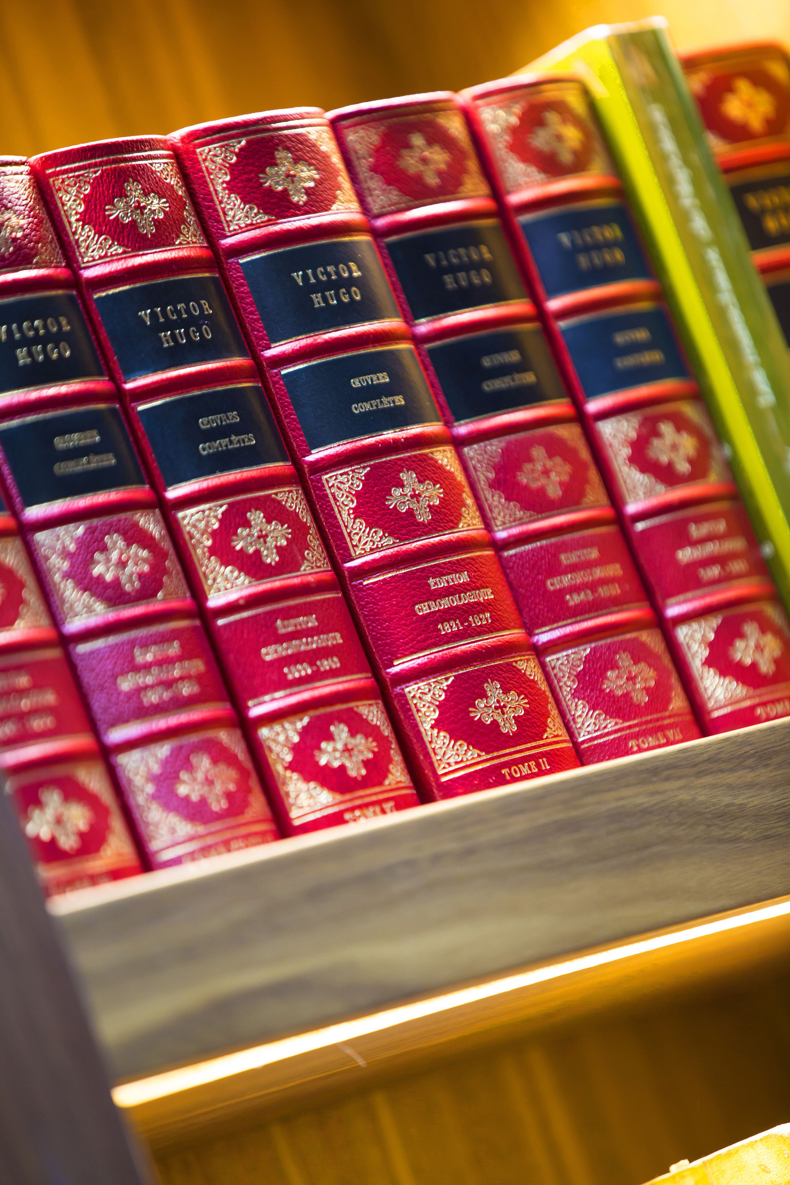 A collection of books with red and gold covers, some labeled 'Victor Hugo'.