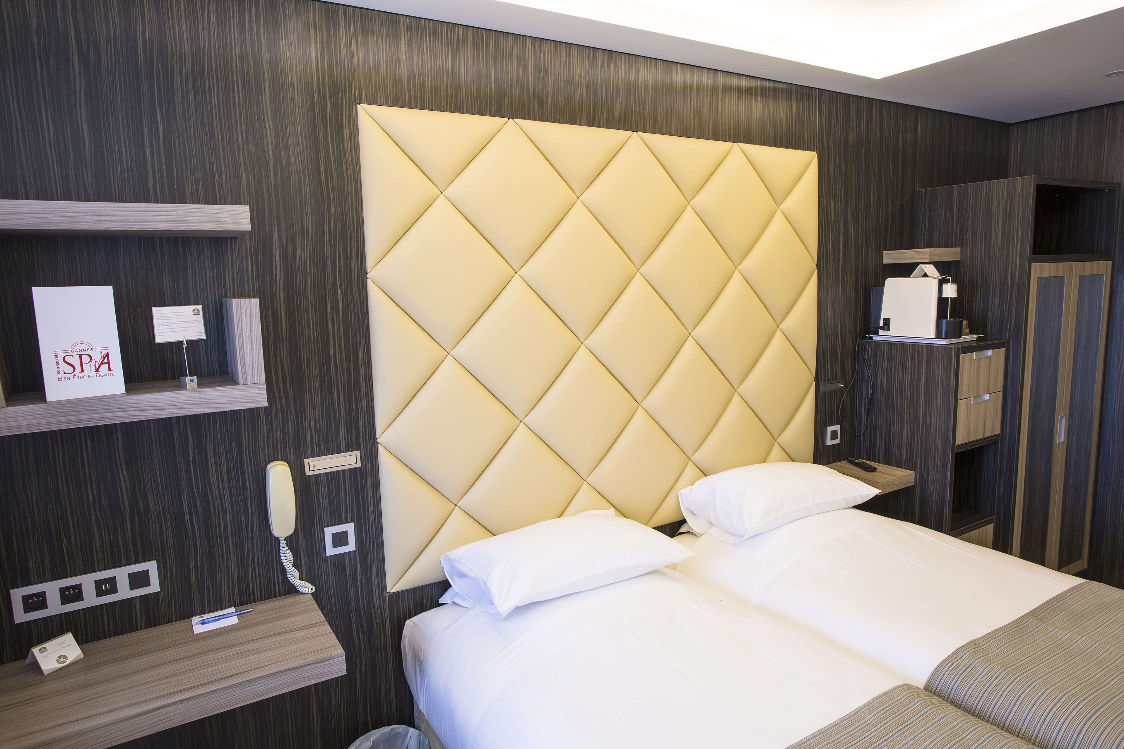 Une chambre d’hôtel avec un grand lit, une table de chevet, un téléphone, un petit bureau avec un ordinateur et un minibar.