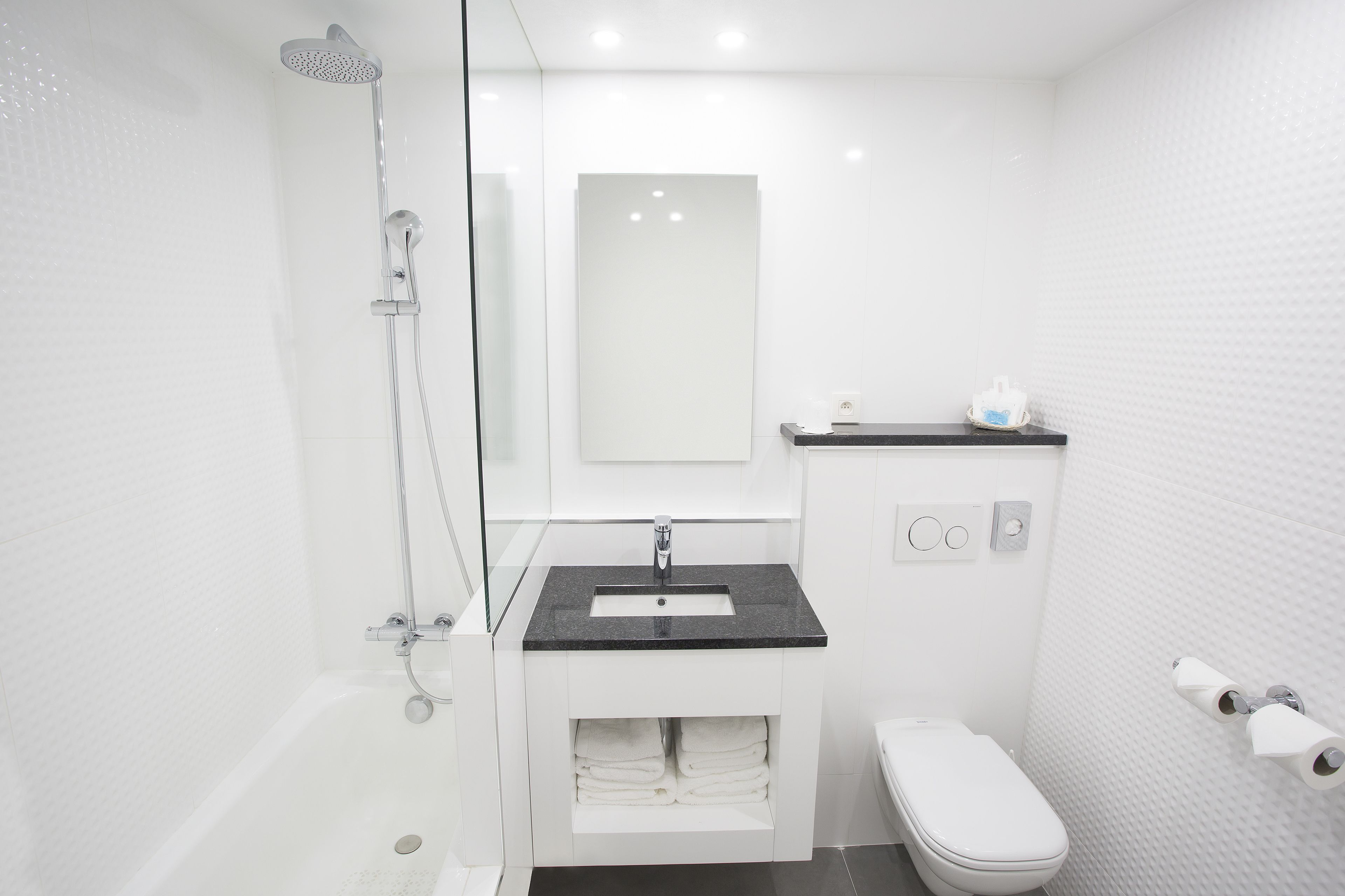 Un bagno moderno con doccia vetrata, lavandino bianco con piano d'appoggio nero, water e porta asciugamani.