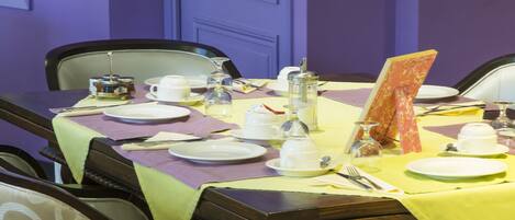 Una mesa de comedor dispuesta con platos, cubiertos y un menú en una habitación con paredes moradas y una puerta.