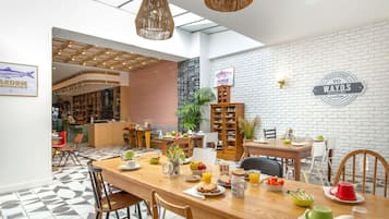 Zona pranzo con un lungo tavolo di legno, sedie e diversi articoli per la colazione. C’è un cartello appeso al muro e una libreria.