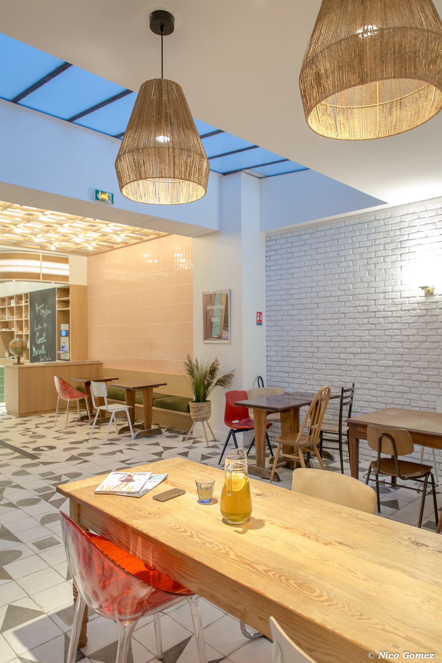 Een modern café met houten tafels en stoelen, een glazen dak en een bakstenen muur.