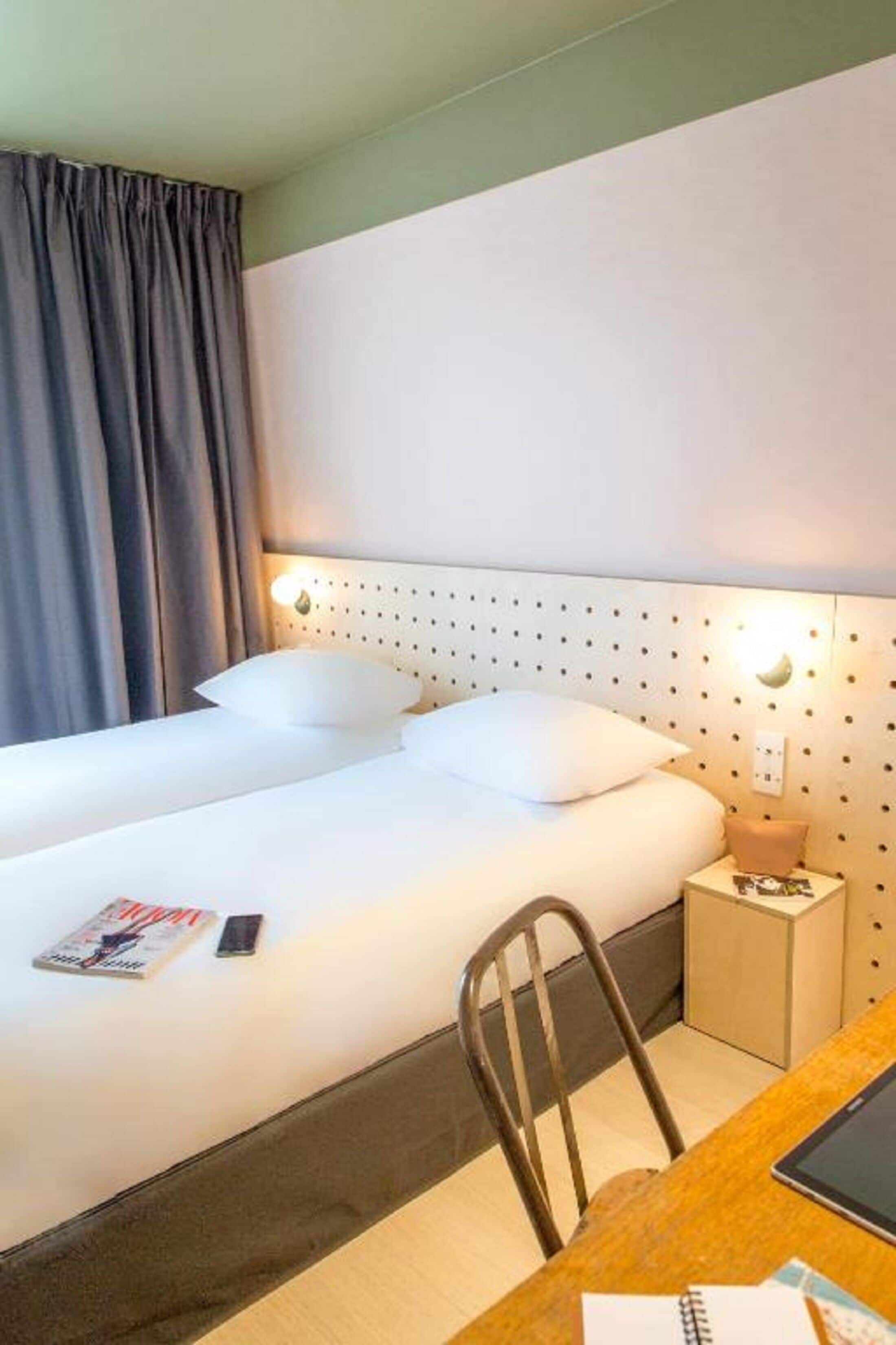 Ett hotellrum med en väl bäddad säng, ett sängbord med en lampa, en stol och ett litet bord med en surfplatta.