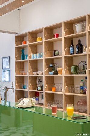 Una habitación con mostrador de recepción verde, estantes de madera con diversos objetos y un teléfono.