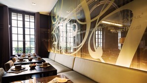 A modern dining area with tables set for a meal, a large decorative wall, and a view through the windows. - Hôtel Chambellan Morgane (Paris)