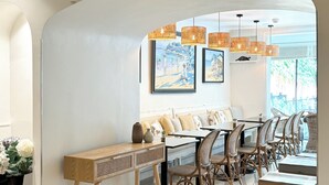 A dining area with wicker furniture, a long table, and hanging wicker lamps.