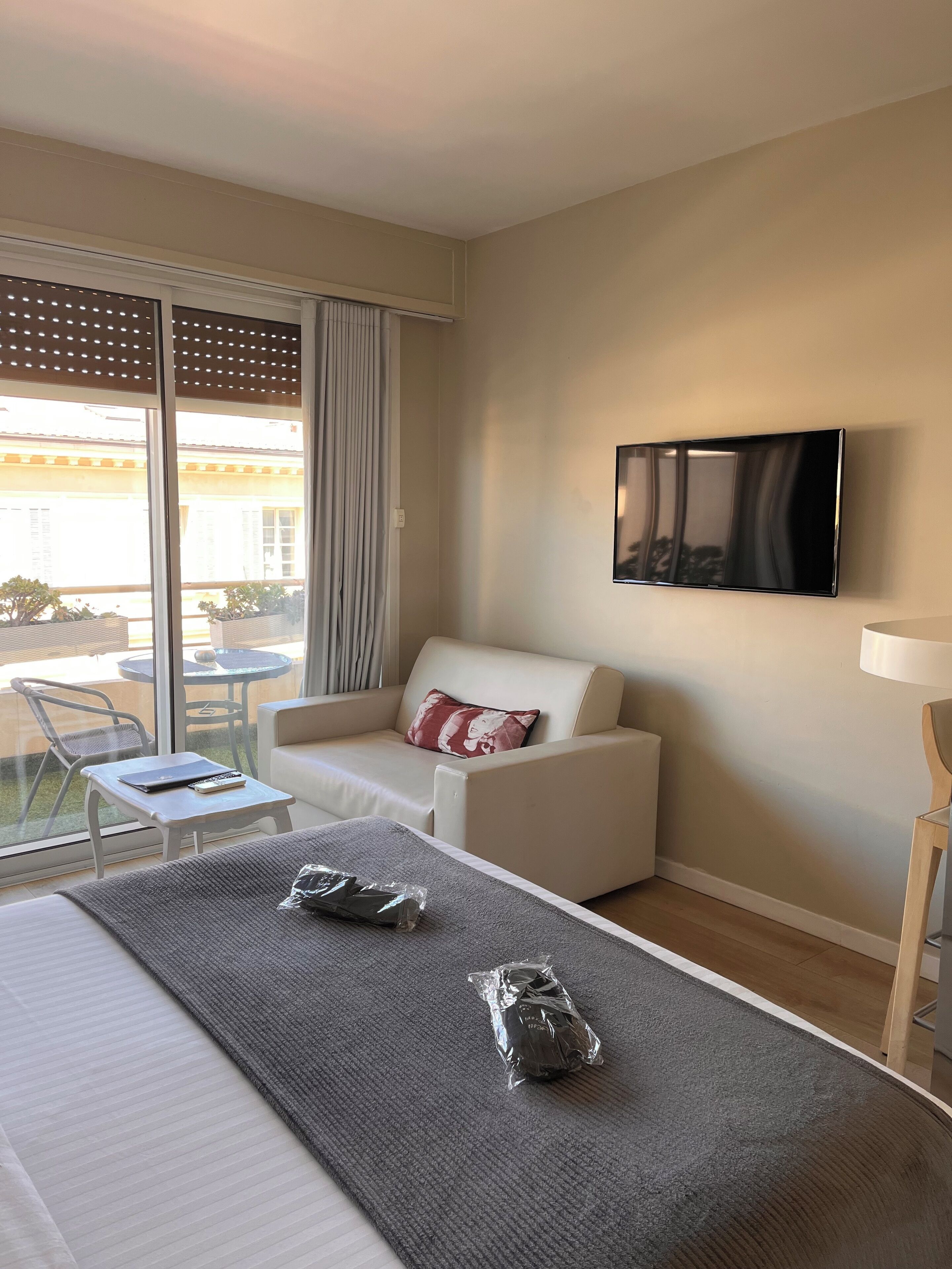 Quarto de hotel com cama, sofá, televisão, mesa pequena e janela com vista para o exterior.
