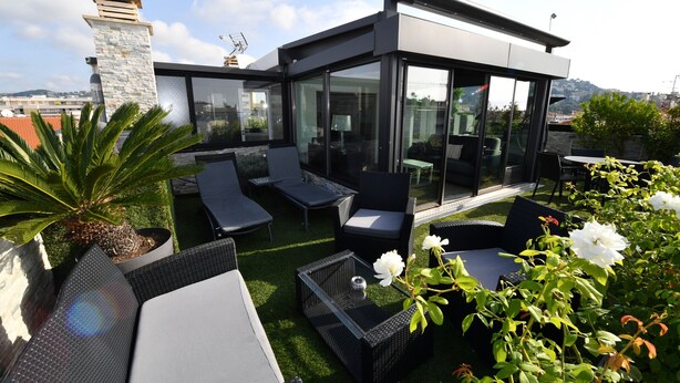 A rooftop terrace with outdoor seating, a stone chimney, and a glass-enclosed area.