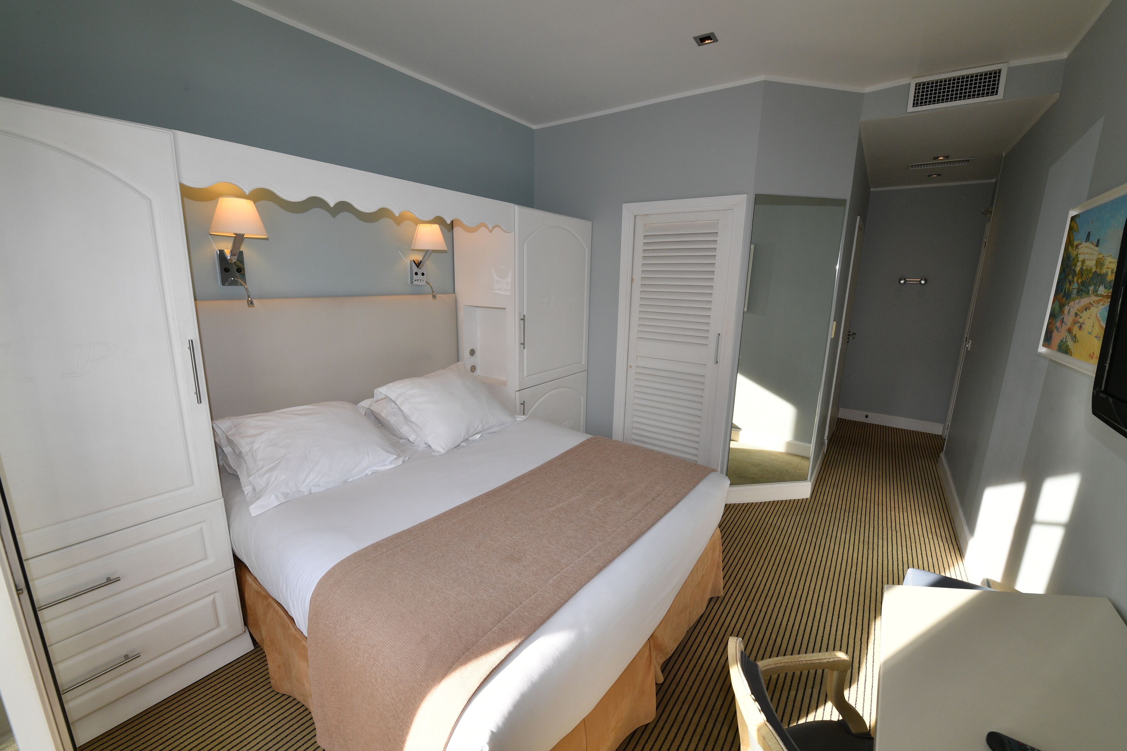 A bedroom with a bed, bedside lamps, a wardrobe, and a door leading to another room.