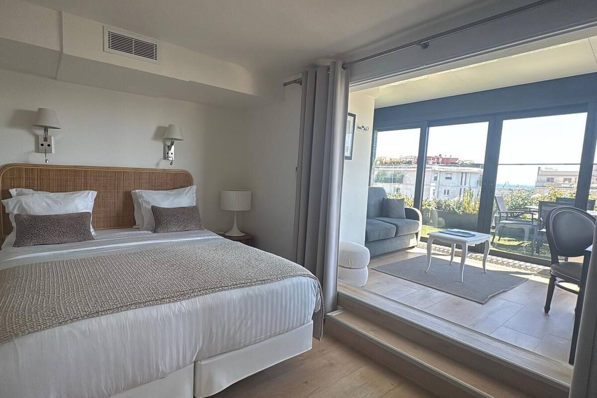 A bedroom with a large bed, bedside lamps, a wooden headboard, and a balcony with outdoor furniture.