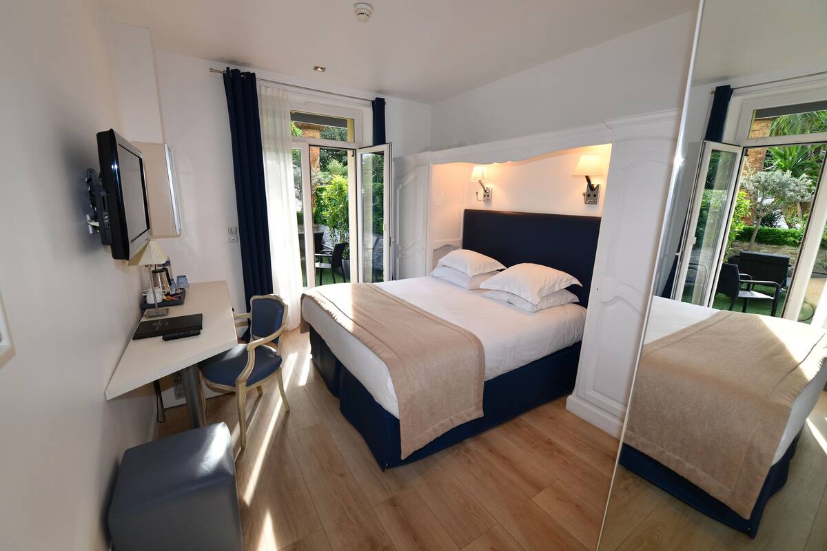A hotel room with a bed, a desk, a chair, a TV, and a large window.