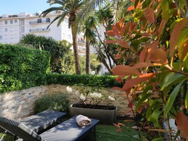 A garden area with a lounge chair, a potted plant with white flowers, and a stone wall.