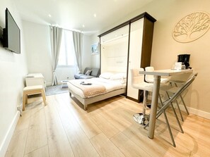 A modern hotel room with a bed, a desk, a chair, a TV, and a window with curtains. - Hotel De Provence (Cannes)