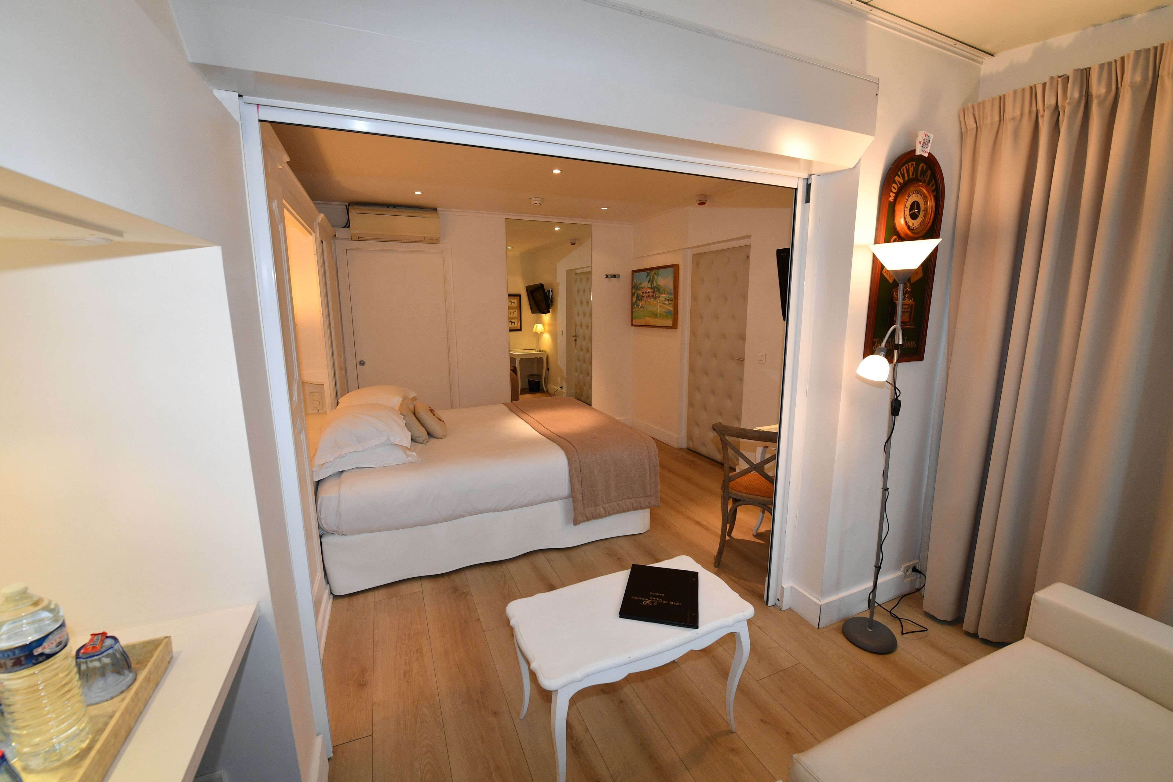 Habitación de hotel con cama, una mesita, una silla, lámpara y dispensador de agua.