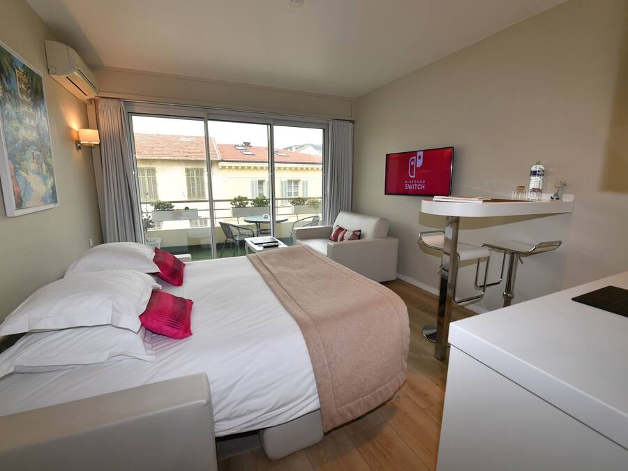 A hotel room with a bed, a desk, a chair, a TV, and a window with a view of buildings.