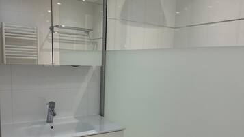 A modern bathroom with a glass shower enclosure, a sink, and a mirror.