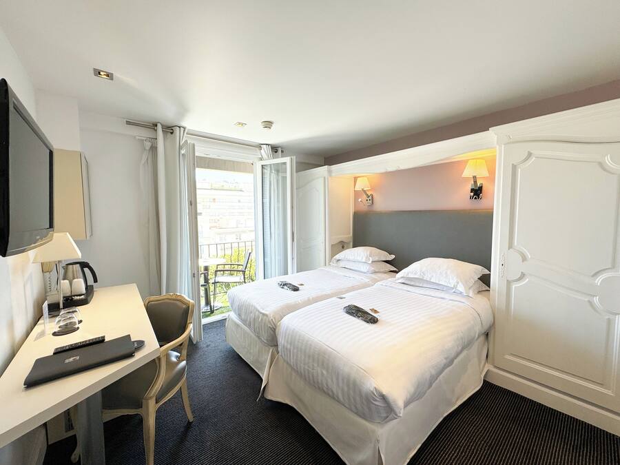 Une chambre d’hôtel avec deux lits, un bureau avec une lampe, une chaise et une vue sur le balcon extérieur.