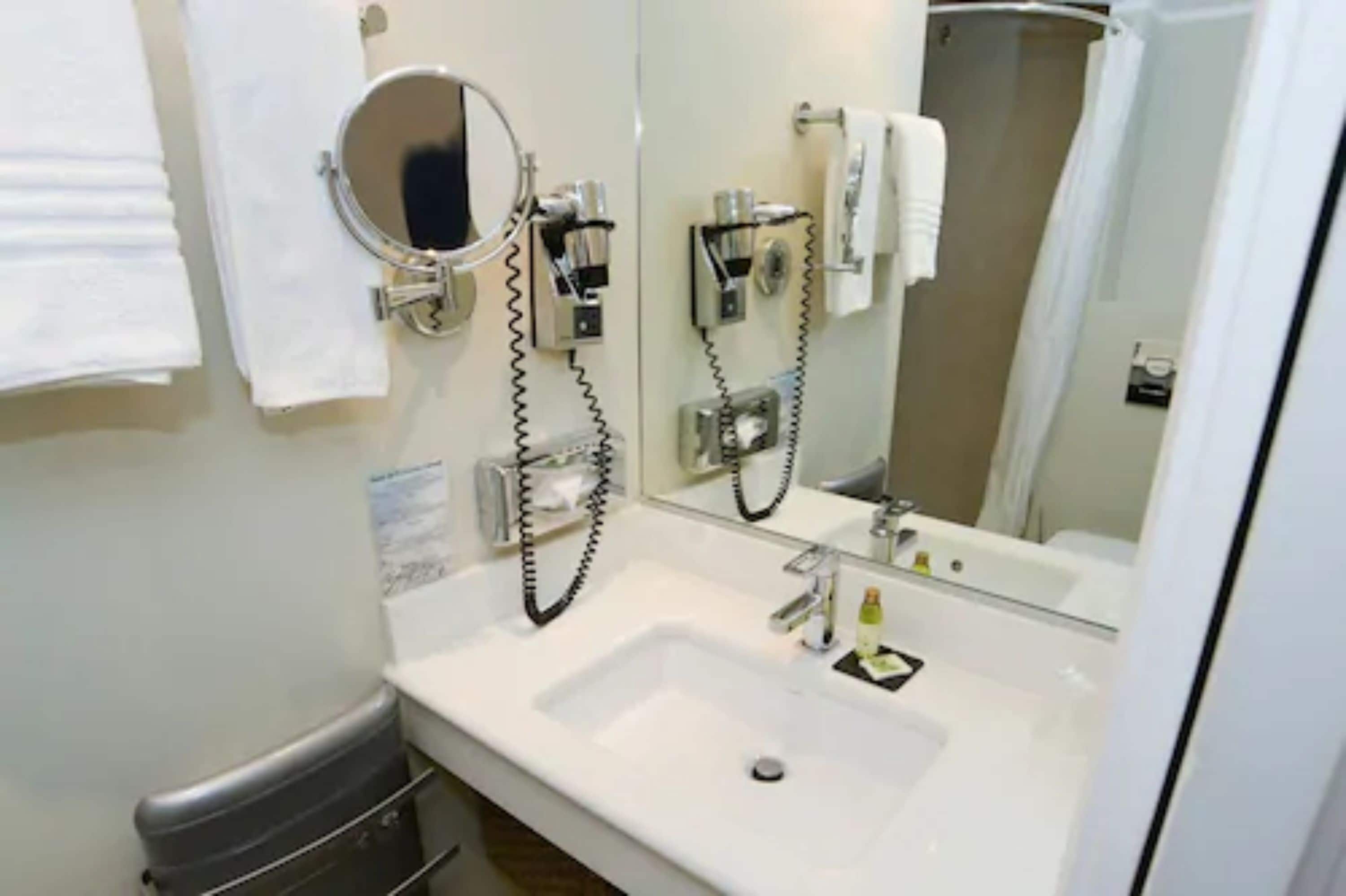 Un baño con un lavamanos blanco, un espejo y un secador de pelo montado en la pared.