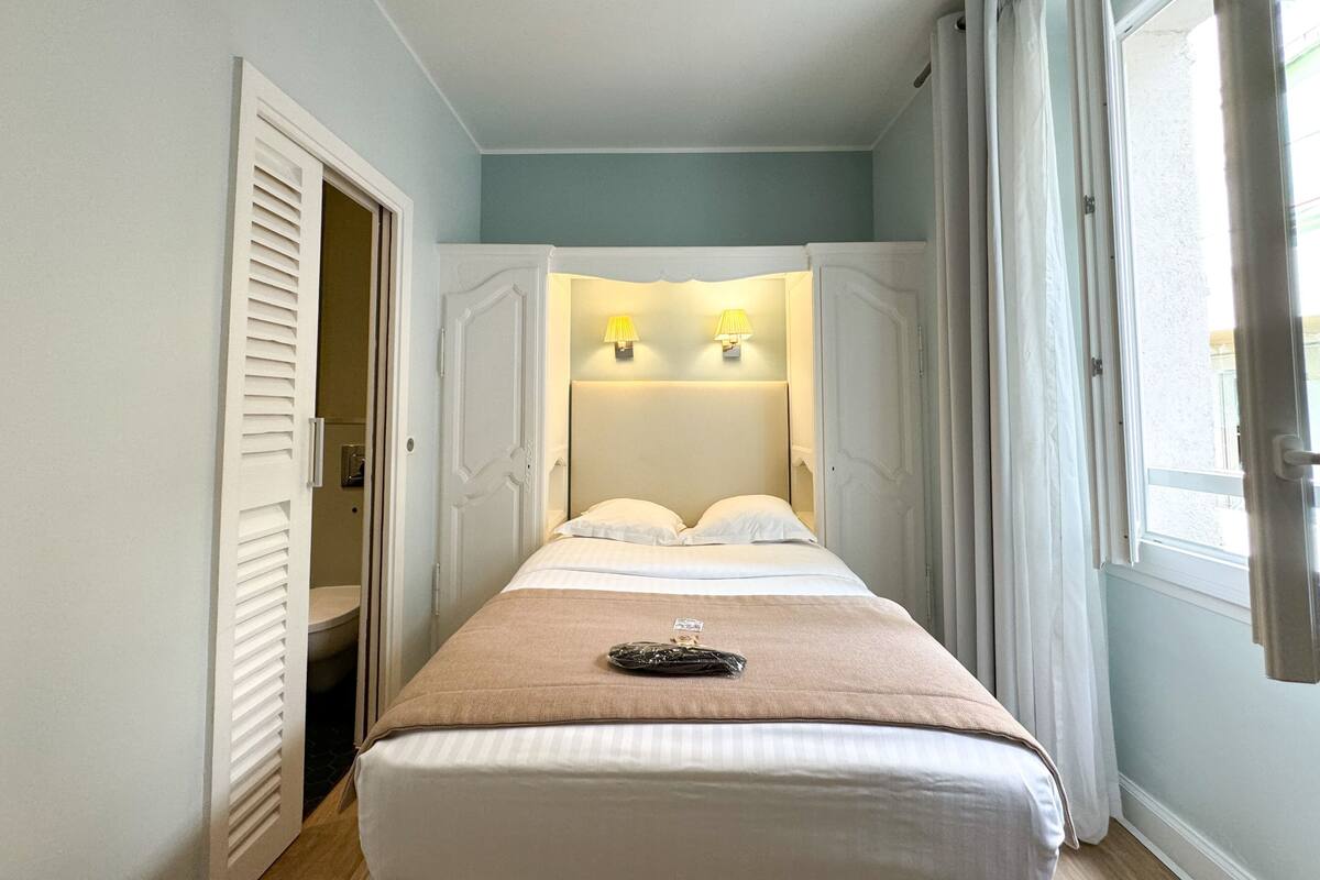 A bedroom with a bed, two bedside lamps, a window, and a door.
