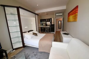 A modern bedroom with a bed, bedside table, and a glass shelving unit.