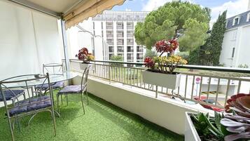 Un balcon avec un revêtement de gazon synthétique, une table en verre, des chaises en métal et des plantes en pot.