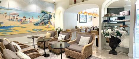A spacious lobby with wicker furniture, a large beach mural, and a view into the dining area.