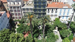 A multi-story hotel with balconies, surrounded by lush greenery and palm trees.
