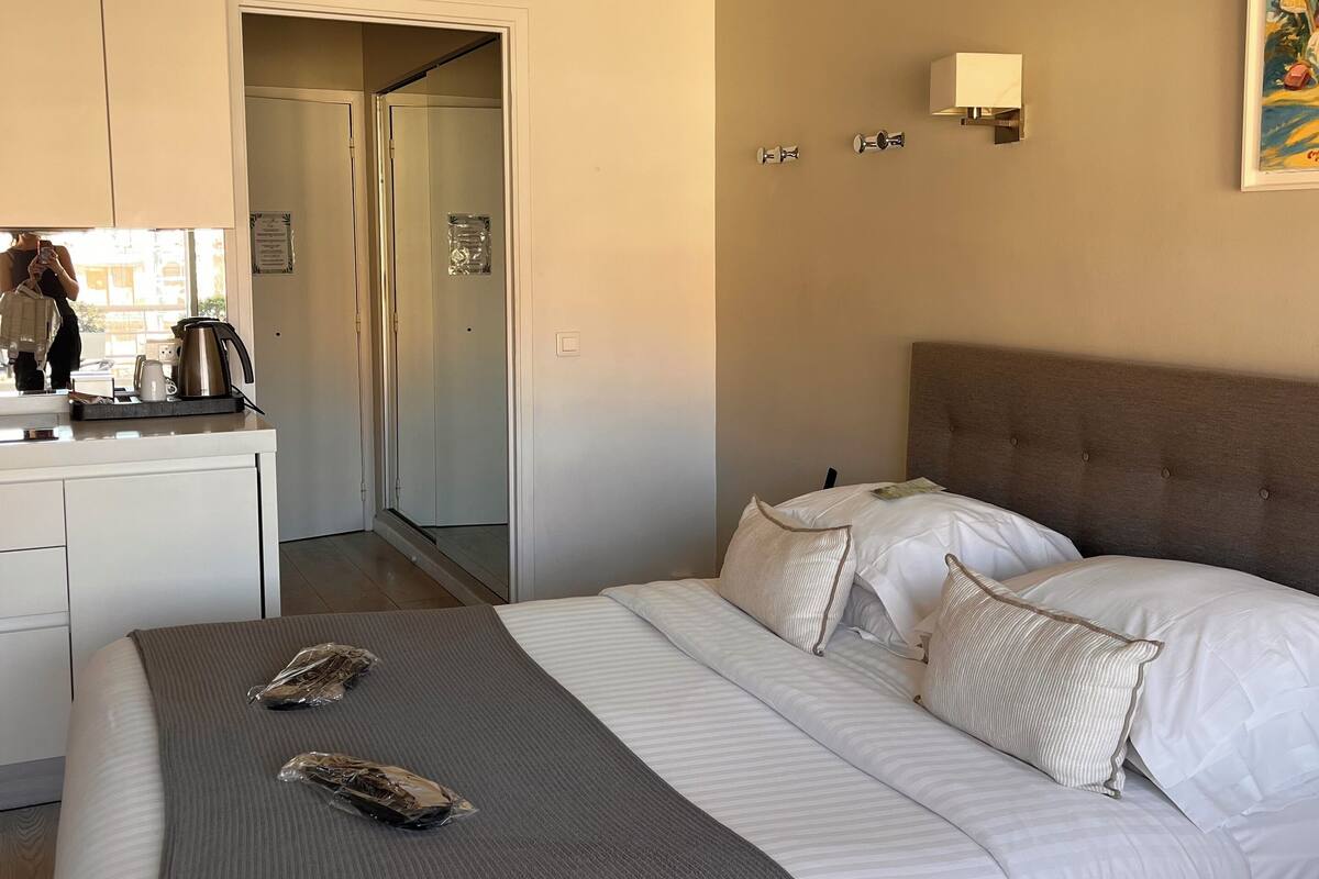 A hotel room with a bed, a bedside table, a coffee maker, and a door leading to a bathroom.