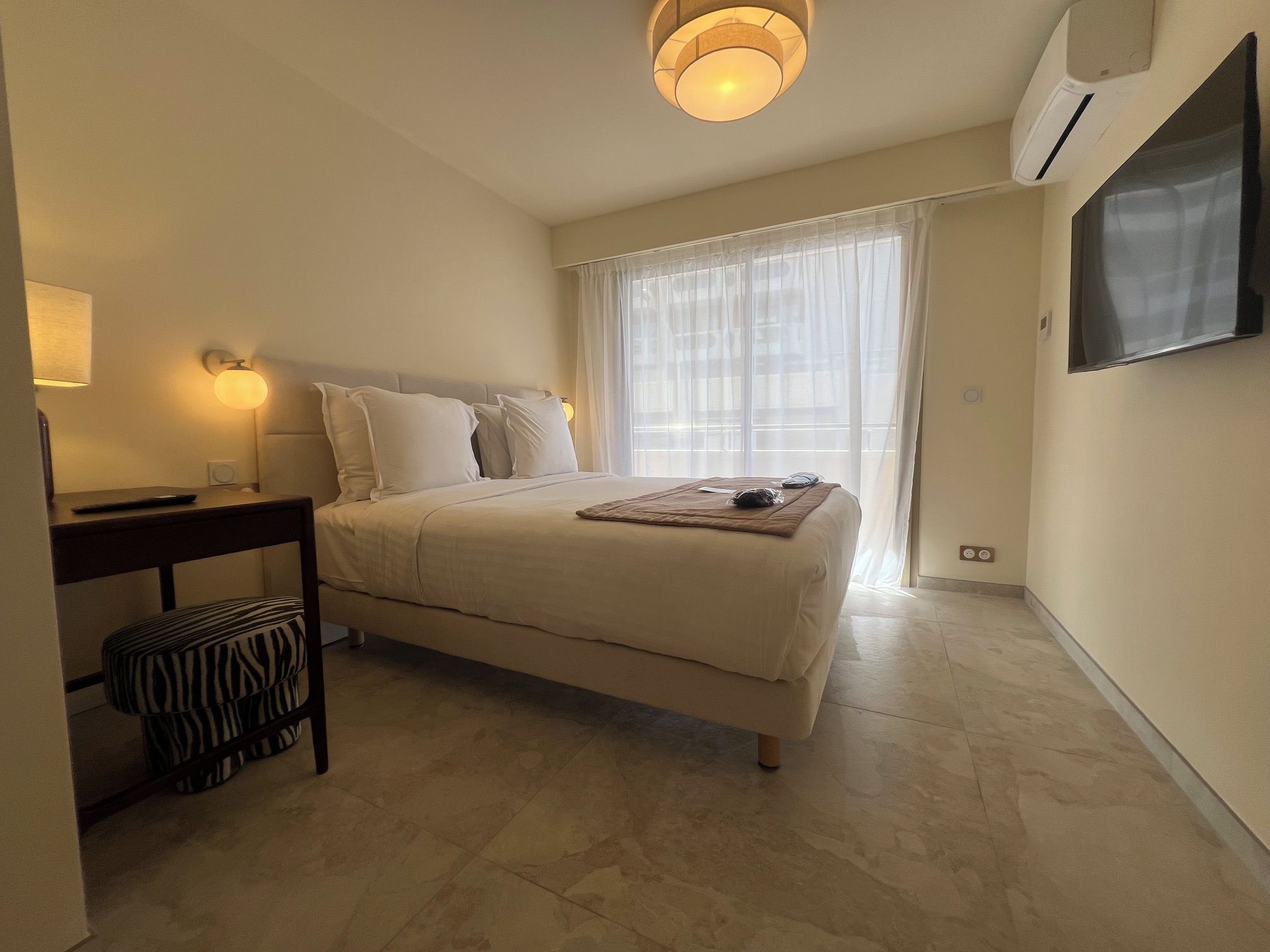 A hotel room with a bed, bedside table, lamp, and a TV mounted on the wall.