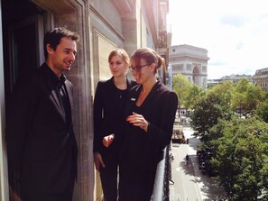 Three people standing on a balcony with a view of the Arc de Triomphe and a tree-lined street below. - Etoile Park Hotel (Paris)