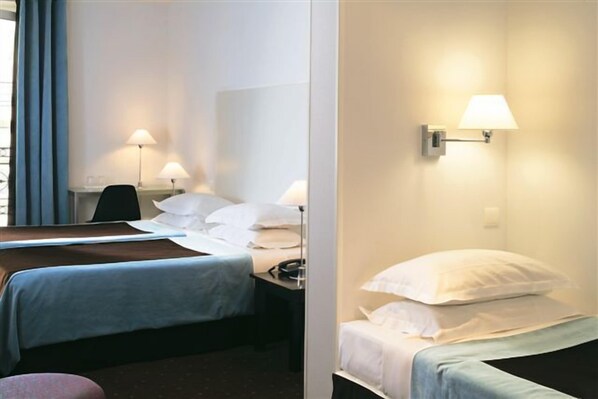 A hotel room with two beds, a desk, and two wall-mounted lamps.