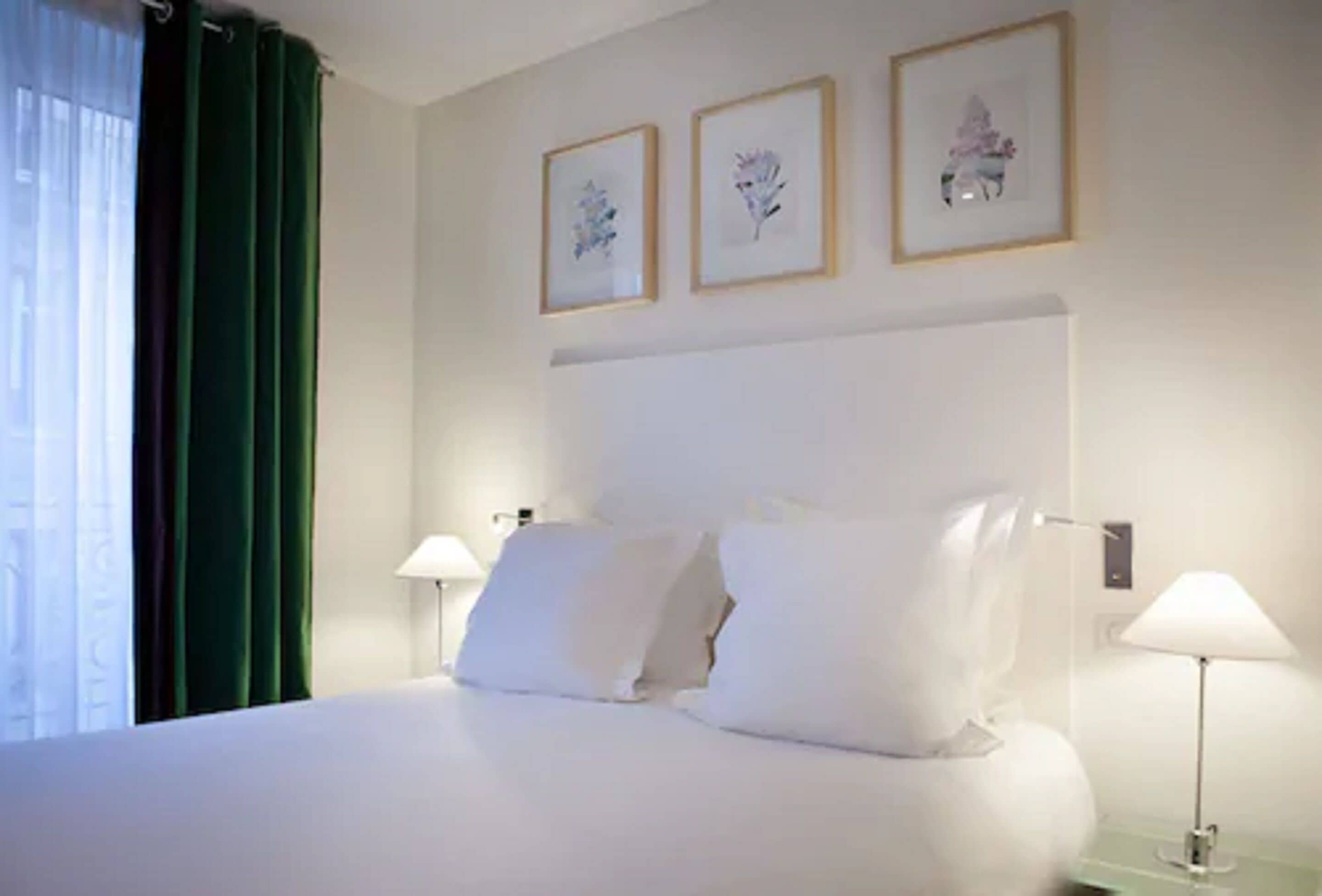 A hotel room with a large bed, two bedside tables, and three framed pictures on the wall.