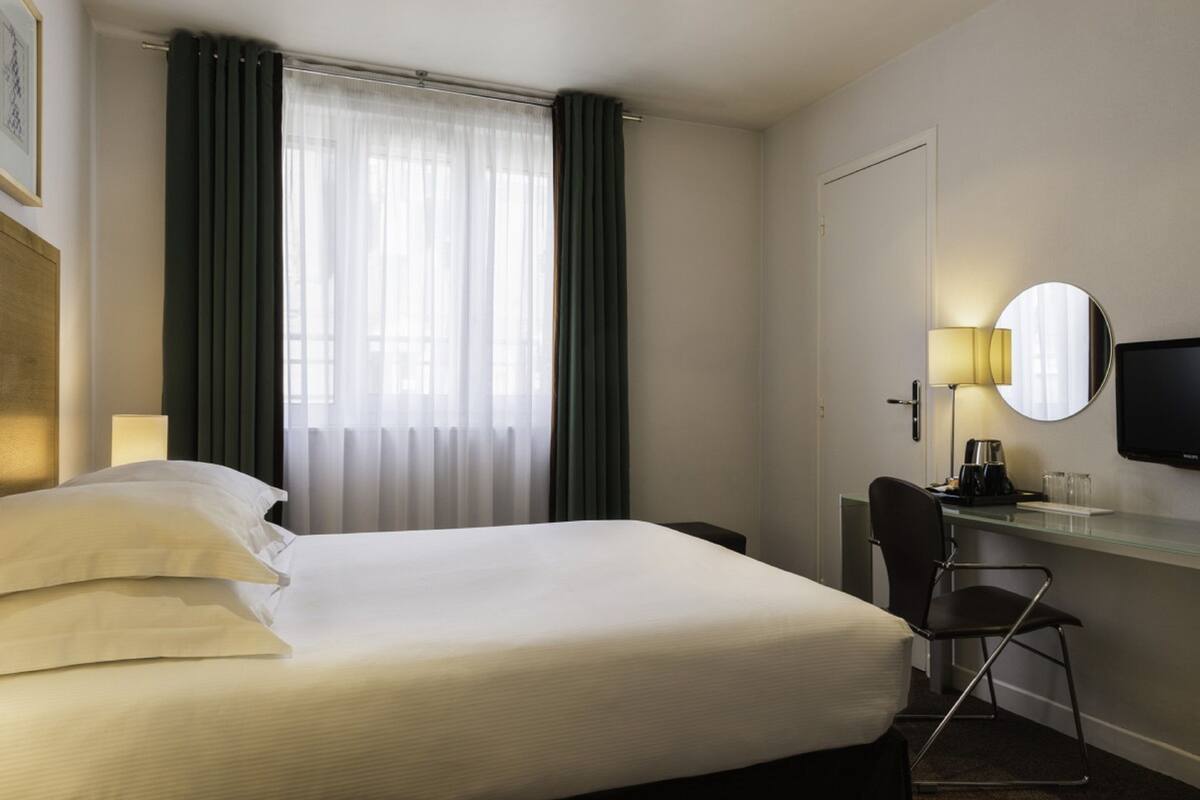 A hotel room with a bed, a desk, a chair, a television, and a window with curtains.