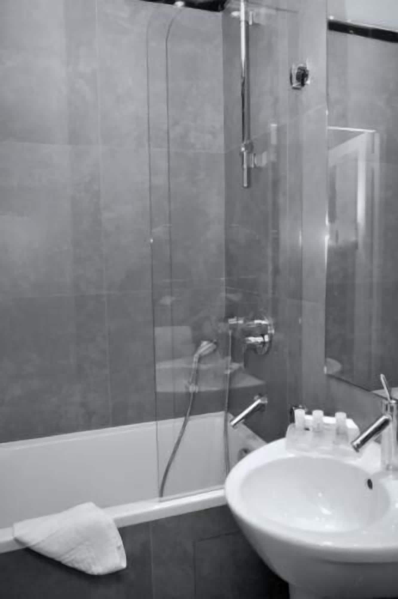 Een badkamer met een douche met glazen wanden, een wastafel met spiegel en een handdoek op de vloer.