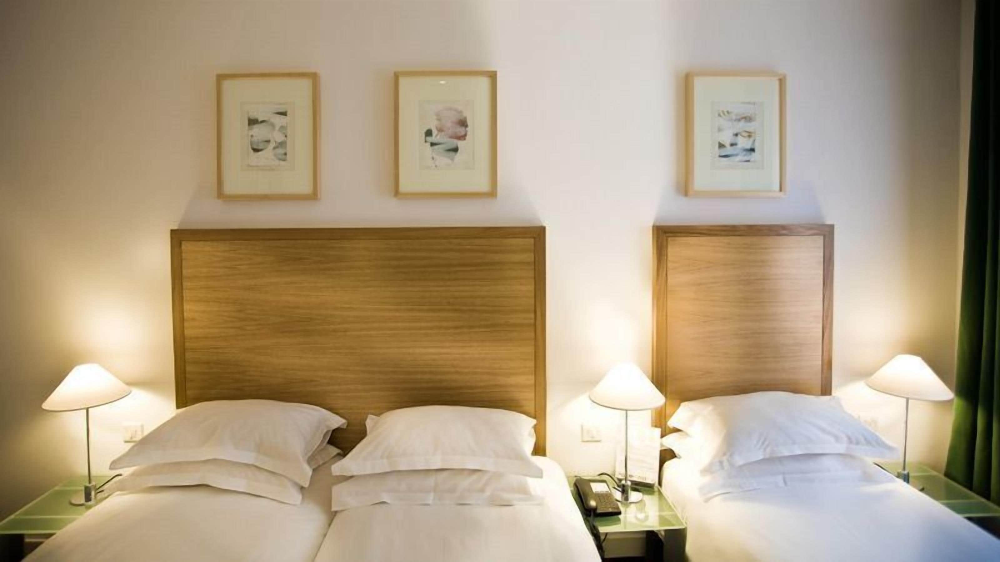 Habitación de hotel con dos camas, cabeceros de madera, lámparas de noche y cuadros en la pared.