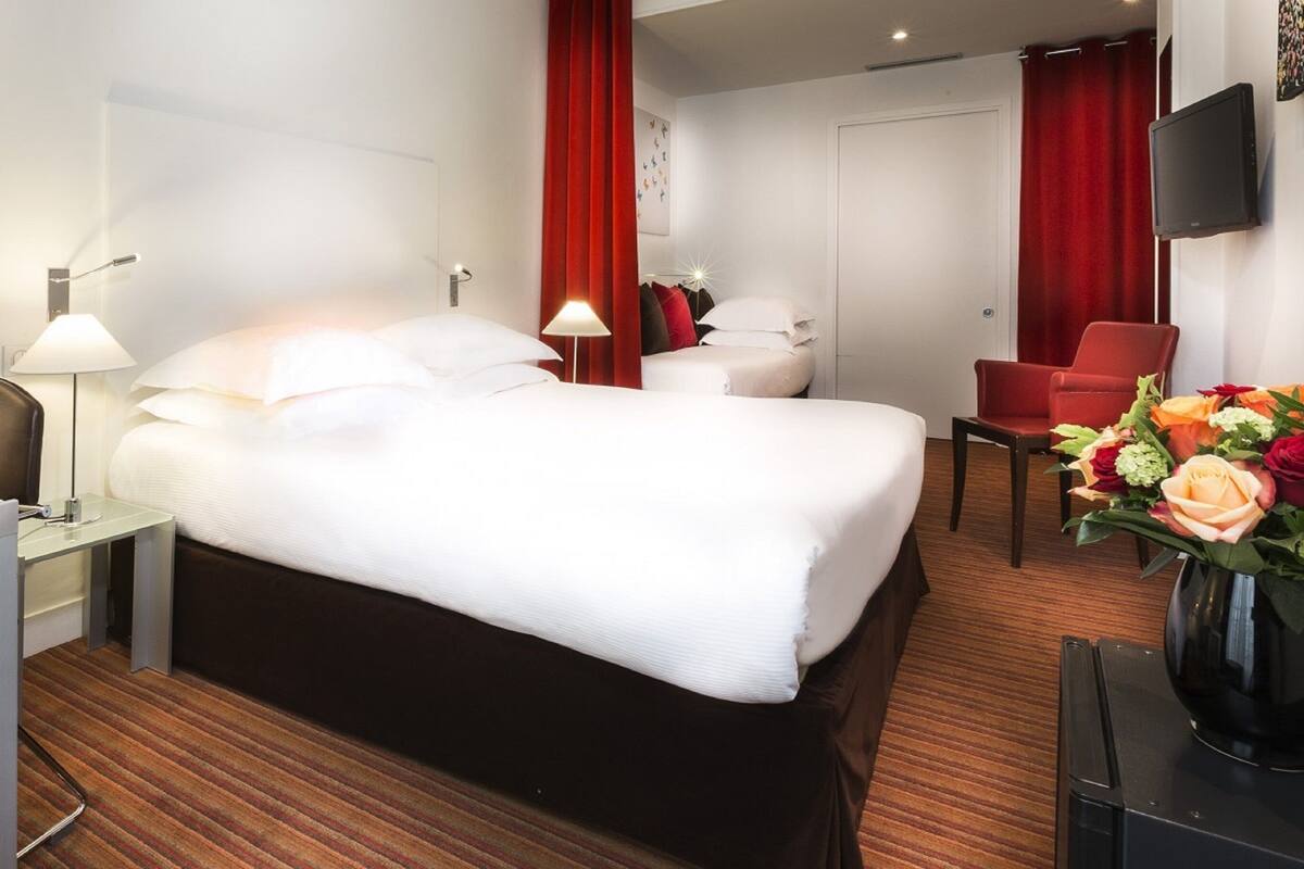 A hotel room with a large bed, a desk with a lamp, a chair, a TV, and a bouquet of flowers.