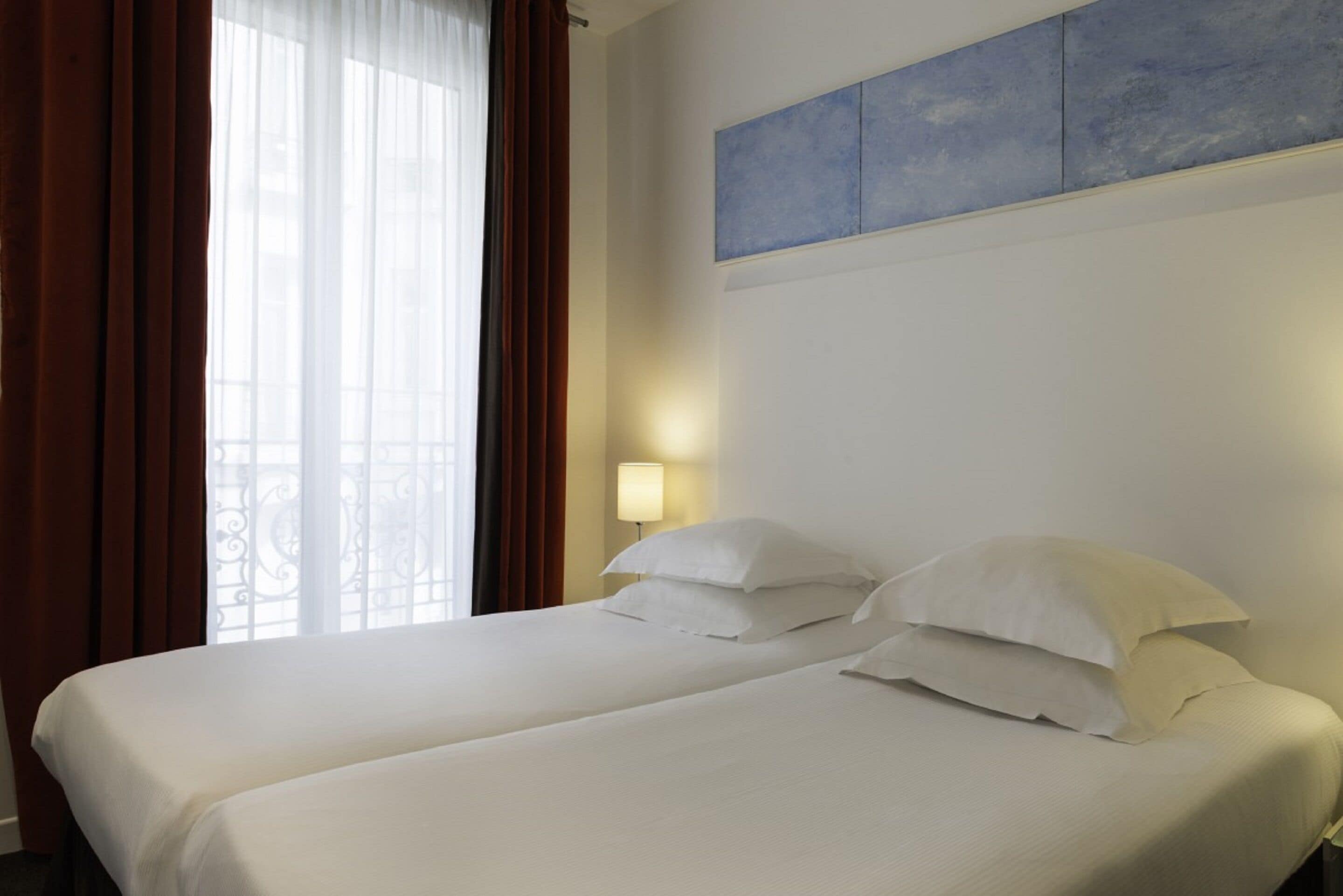 A hotel room with a bed, curtains, a wall-mounted light, and a window with a view.