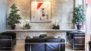 A modern lobby with black leather sofas, a stone wall, and a framed abstract painting. - Albe Hôtel Saint-Michel (Paris)