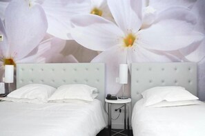 Ein Hotelzimmer mit zwei Betten, einem runden Beistelltisch, einer Nachttischlampe und einer Wand mit einer großen Blumenmalerei.