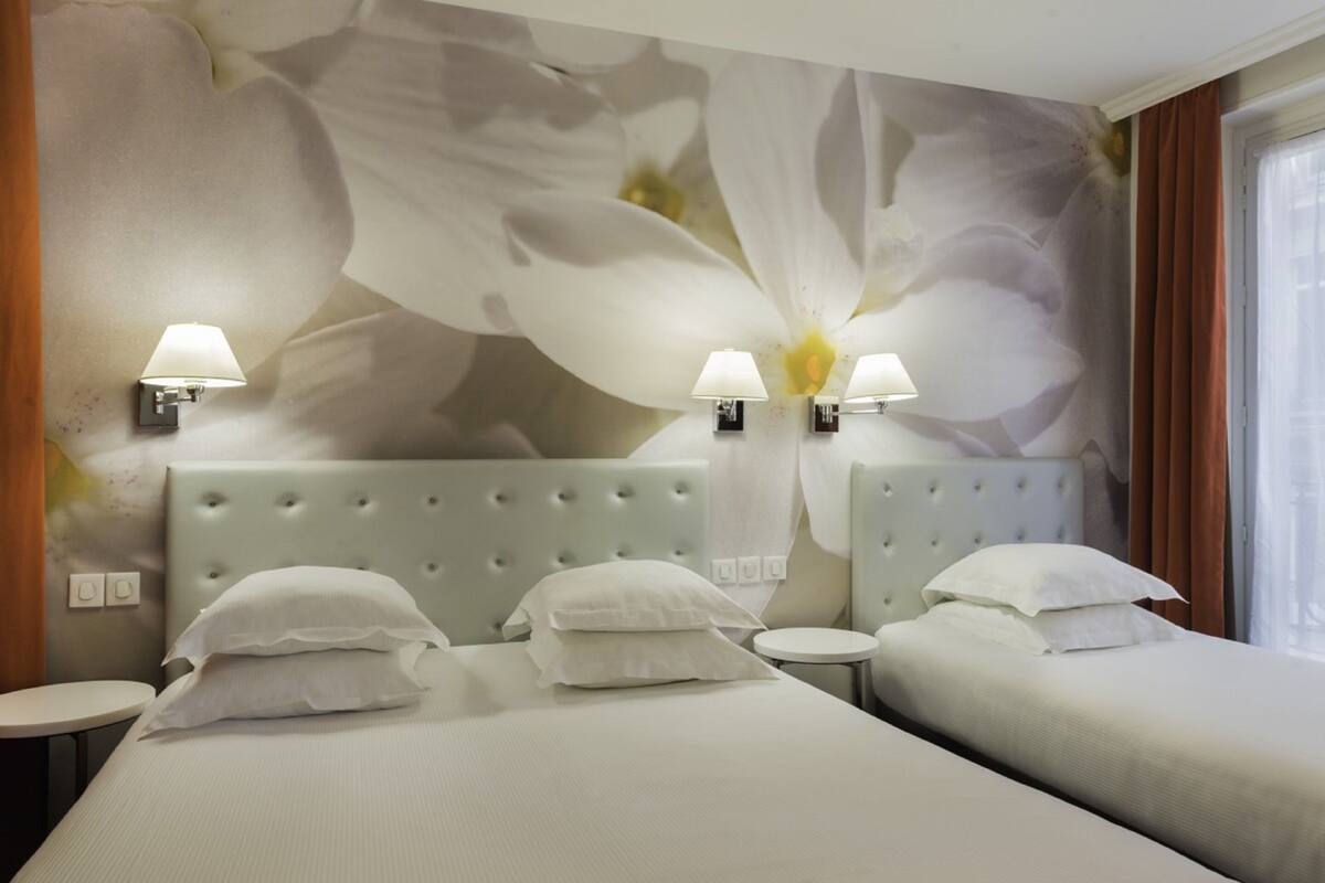 A hotel room with a large floral mural, two beds with white linens, two bedside lamps, and a round table.